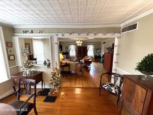 hallway featuring wood-type flooring, crown molding, plenty of natural light, and a notable chandelier