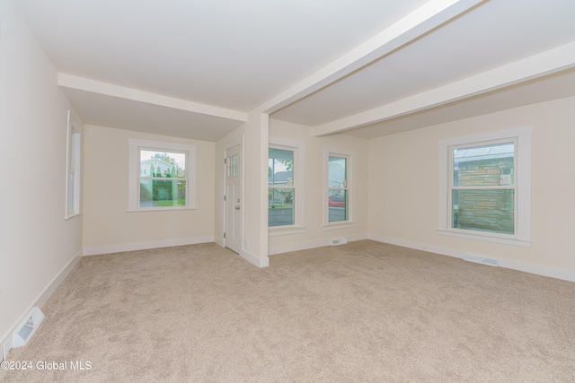 spare room featuring light colored carpet and beamed ceiling