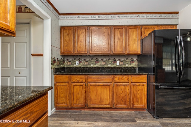 kitchen featuring black refrigerator, dark hardwood / wood-style flooring, dark stone countertops, and tasteful backsplash