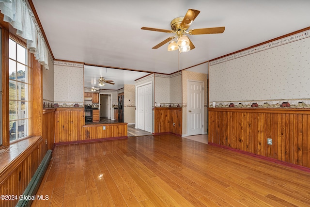 unfurnished living room with wood-type flooring, baseboard heating, crown molding, and ceiling fan