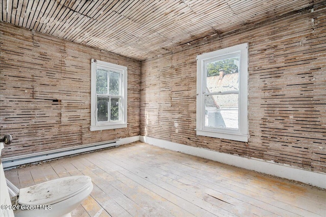 spare room featuring a baseboard heating unit, light hardwood / wood-style floors, and wooden walls