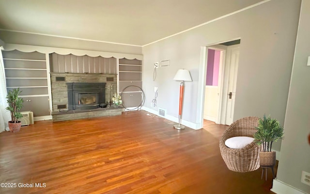 living area with wood finished floors, baseboards, built in shelves, and a glass covered fireplace