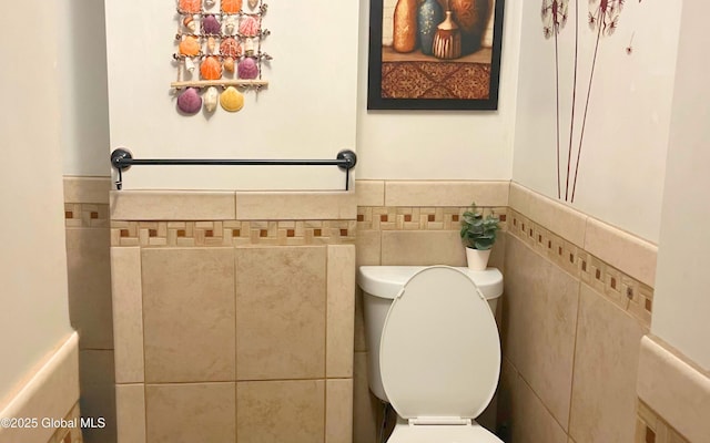 bathroom with tile walls, toilet, and a wainscoted wall
