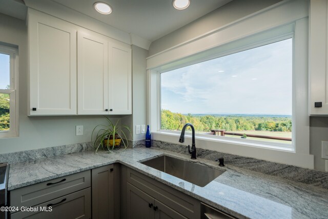 kitchen with white cabinetry, sink, and light stone counters