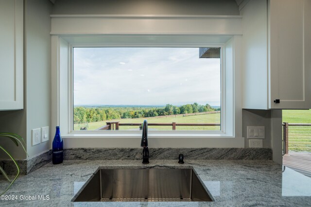 interior details with light stone counters, sink, and white cabinets