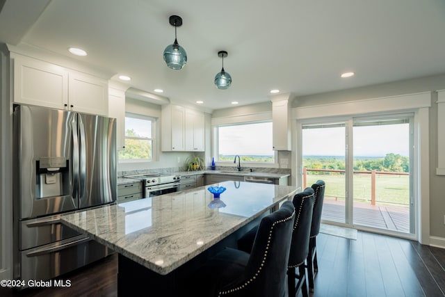 kitchen with white cabinetry, hanging light fixtures, stainless steel appliances, a kitchen breakfast bar, and a kitchen island