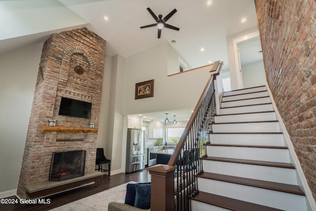 stairs featuring hardwood / wood-style flooring, ceiling fan, a brick fireplace, and a high ceiling