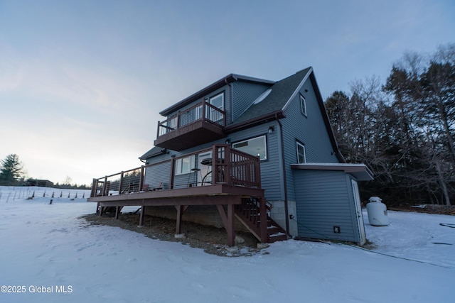 snow covered back of property featuring a balcony and a deck