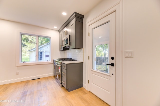 kitchen featuring gray cabinets, light wood-type flooring, appliances with stainless steel finishes, and tasteful backsplash