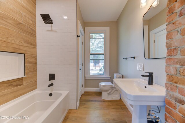 bathroom with hardwood / wood-style flooring, tiled shower / bath, and toilet