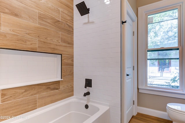 bathroom featuring wood-type flooring, tiled shower / bath, and toilet