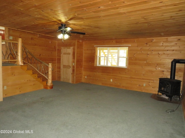 unfurnished living room with wood ceiling, a wood stove, ceiling fan, and carpet flooring