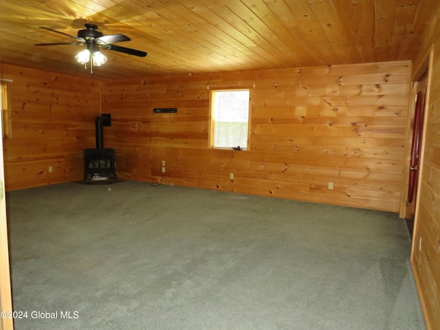 spare room featuring ceiling fan, wood ceiling, carpet flooring, and a wood stove