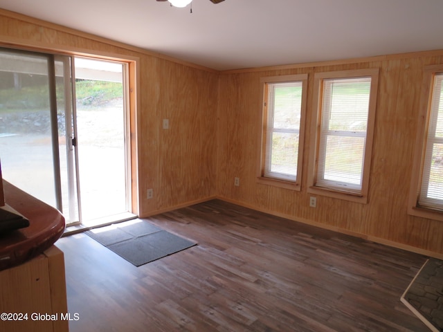 empty room with wood walls, ceiling fan, and dark wood-type flooring