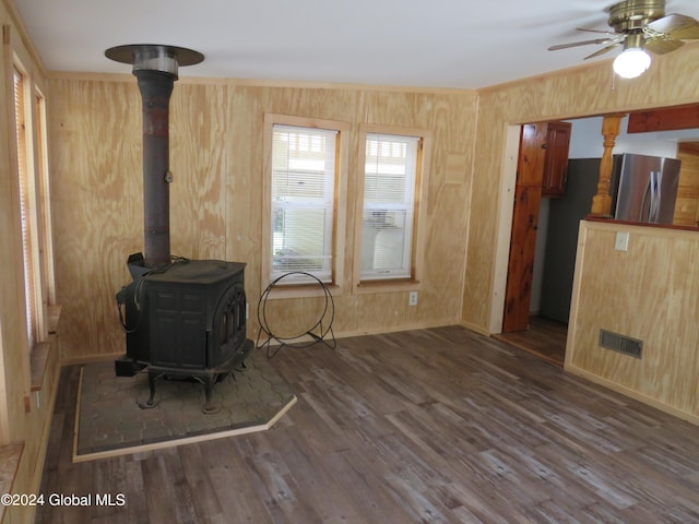 unfurnished living room featuring wood walls, dark hardwood / wood-style flooring, ceiling fan, and a wood stove