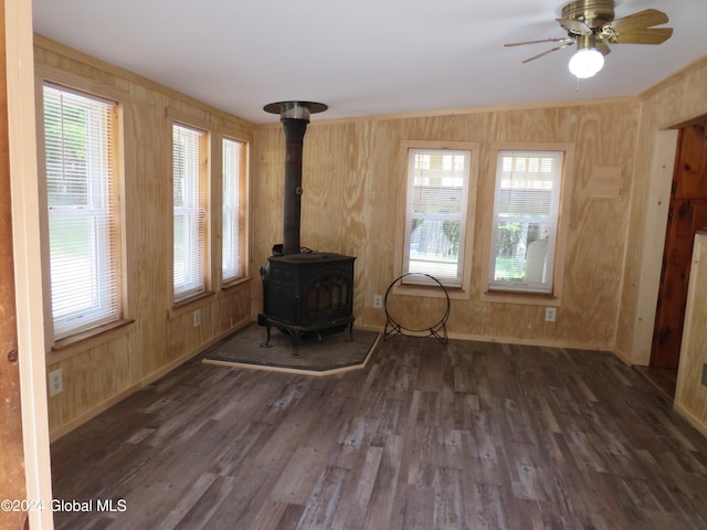 unfurnished living room with wooden walls, dark hardwood / wood-style floors, ceiling fan, and a wood stove