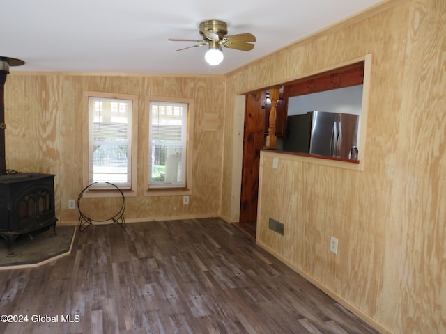 unfurnished living room with wooden walls, dark hardwood / wood-style flooring, ceiling fan, and a wood stove