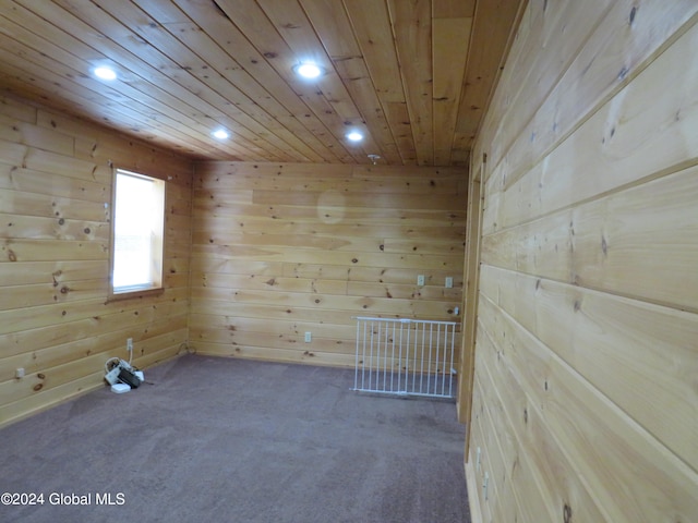 empty room featuring wood ceiling, wooden walls, and dark carpet