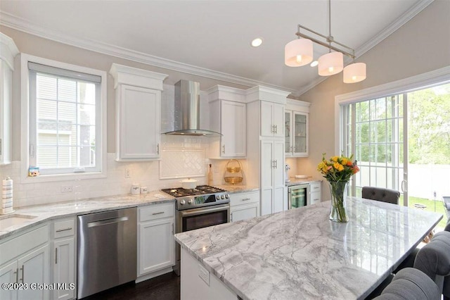 kitchen featuring stainless steel appliances, decorative light fixtures, plenty of natural light, and wall chimney range hood