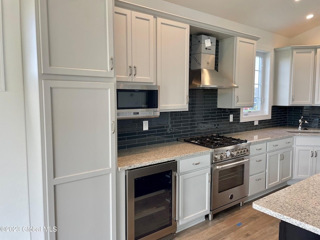 kitchen with white cabinets, beverage cooler, stainless steel appliances, and wall chimney range hood