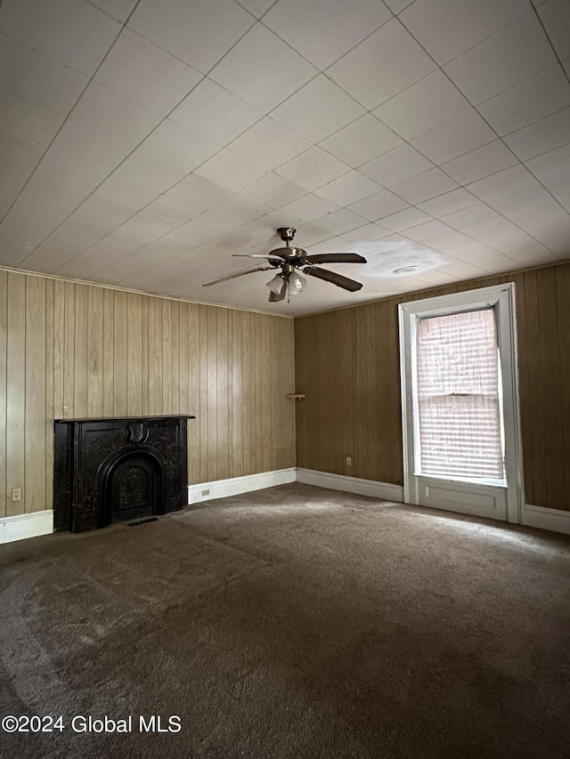 unfurnished living room featuring carpet flooring, wood walls, and ceiling fan