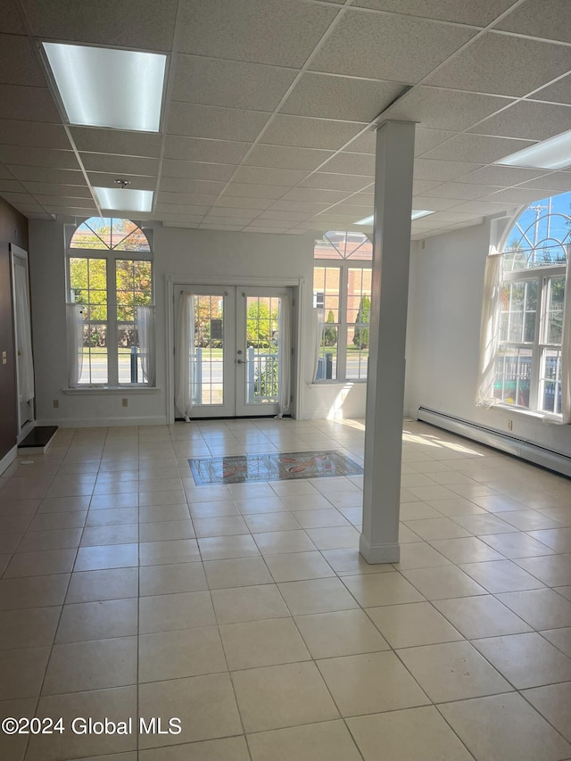 empty room with french doors, a baseboard radiator, a drop ceiling, and light tile patterned floors