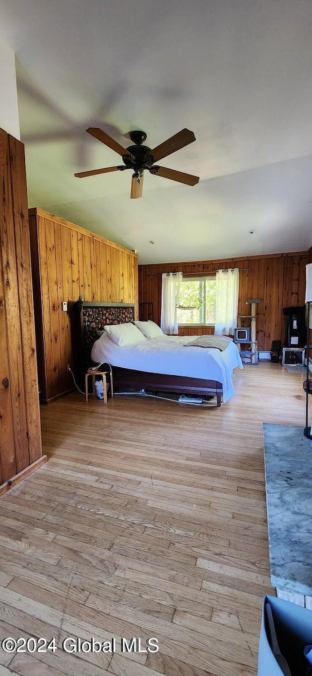 unfurnished bedroom with ceiling fan, wood walls, and light hardwood / wood-style flooring