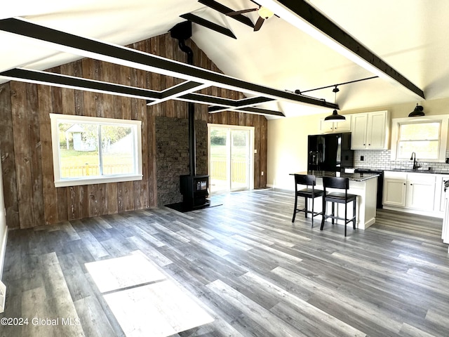 living room featuring ceiling fan, lofted ceiling with beams, a wood stove, wood finished floors, and wooden walls