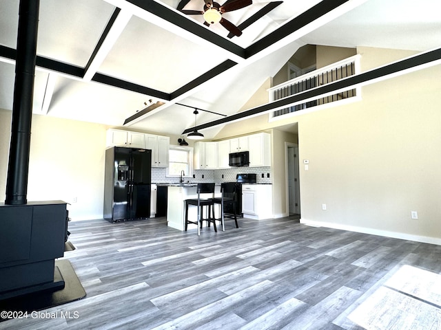 living room featuring a wood stove, ceiling fan, beamed ceiling, light wood finished floors, and high vaulted ceiling