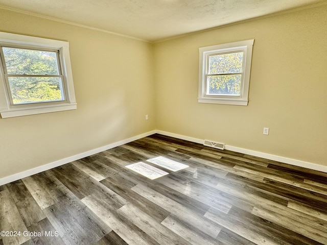 empty room with dark wood finished floors, visible vents, ornamental molding, and a healthy amount of sunlight