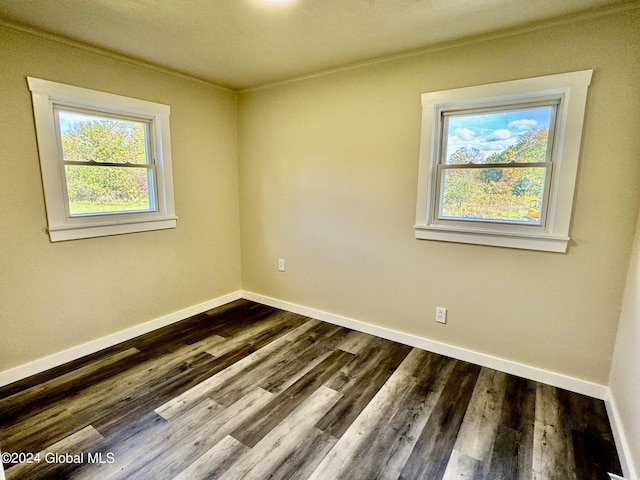empty room featuring dark wood-type flooring, crown molding, and baseboards