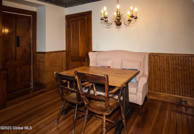 dining area with a chandelier, wood walls, and dark wood-type flooring