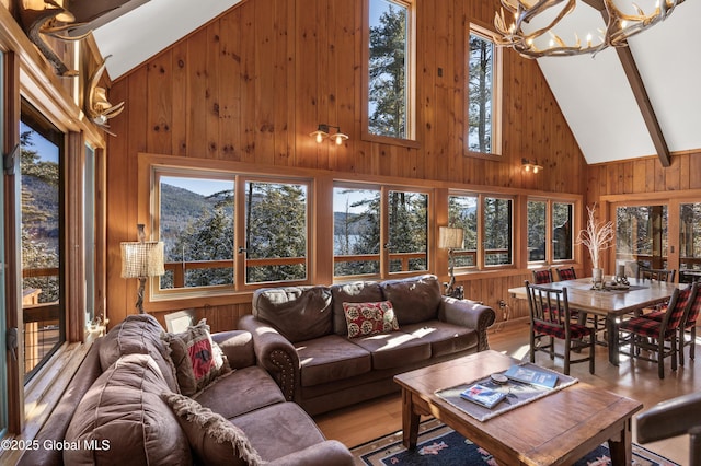 living room featuring a notable chandelier, light wood-type flooring, wood walls, and high vaulted ceiling