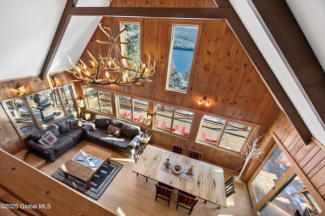 living room with wooden walls, a water view, beamed ceiling, a notable chandelier, and high vaulted ceiling