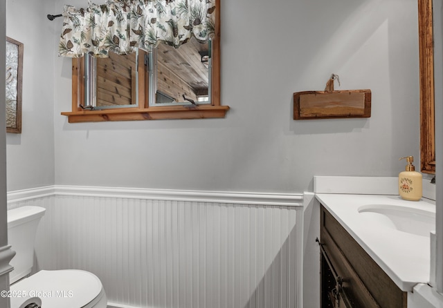 half bath with wainscoting, toilet, and vanity