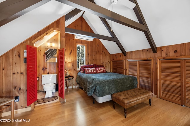 bedroom featuring connected bathroom, wooden walls, wood finished floors, and vaulted ceiling with beams