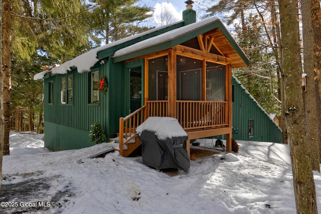 exterior space with board and batten siding, a chimney, and a sunroom