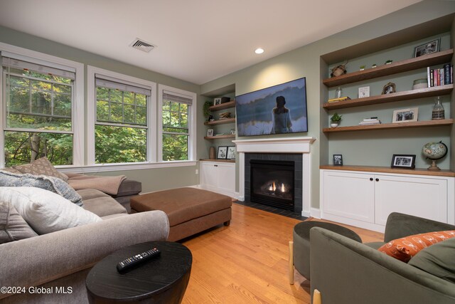 living room with built in shelves, a fireplace, light hardwood / wood-style floors, and a healthy amount of sunlight