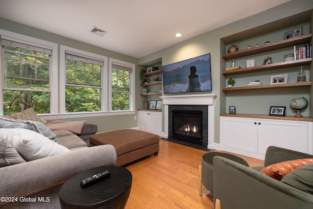 living room with visible vents, a tiled fireplace, light wood-style flooring, and built in features