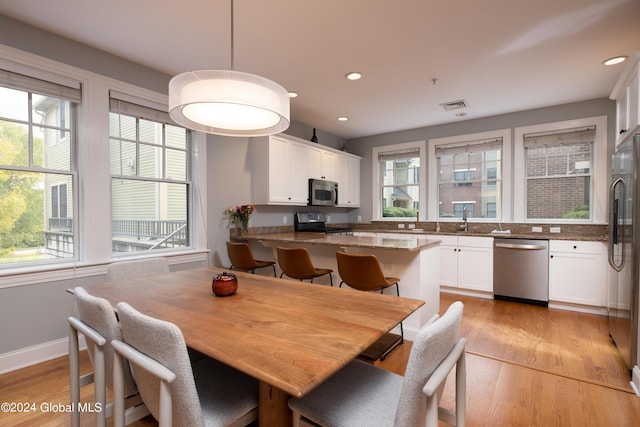 kitchen with white cabinets, stainless steel appliances, a healthy amount of sunlight, and light wood-type flooring