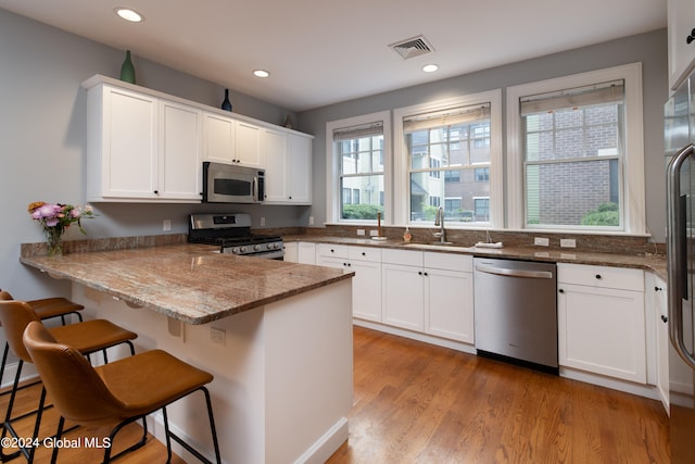 kitchen with appliances with stainless steel finishes, white cabinets, kitchen peninsula, a kitchen bar, and stone counters