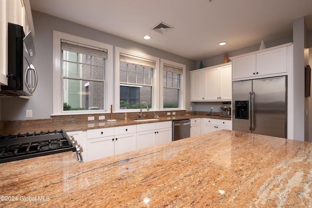 kitchen with a sink, appliances with stainless steel finishes, light stone counters, and visible vents