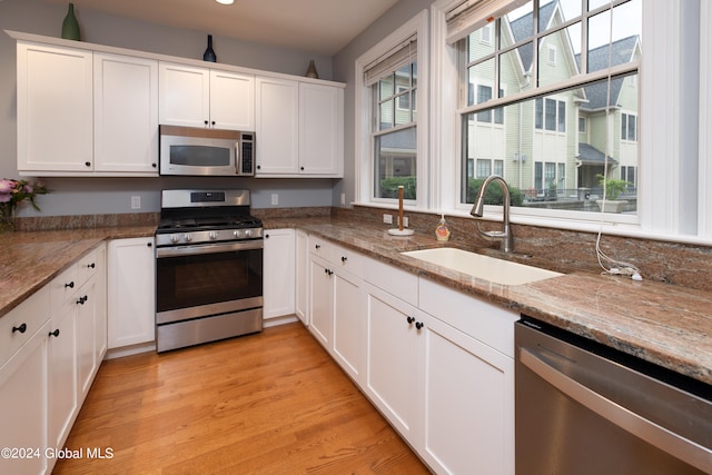 kitchen with stainless steel appliances, white cabinetry, light wood-type flooring, and sink