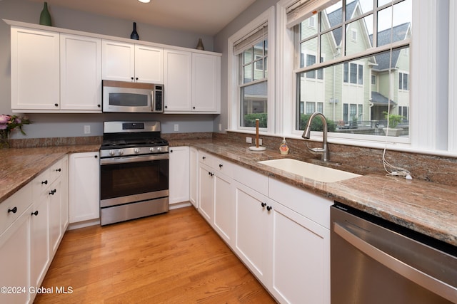 kitchen featuring light stone counters, a sink, white cabinetry, light wood-type flooring, and stainless steel appliances