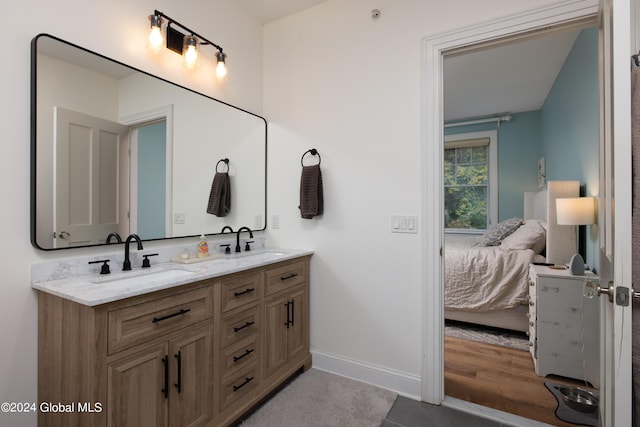 ensuite bathroom with double vanity, ensuite bath, baseboards, and a sink