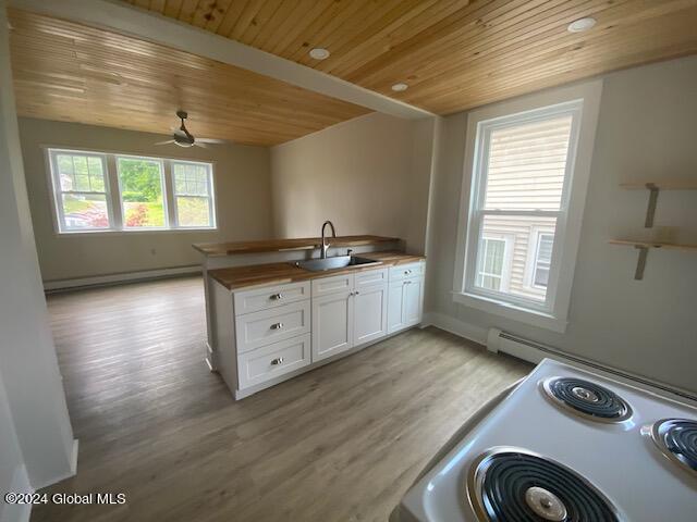 kitchen featuring light hardwood / wood-style floors, white cabinets, baseboard heating, stove, and sink