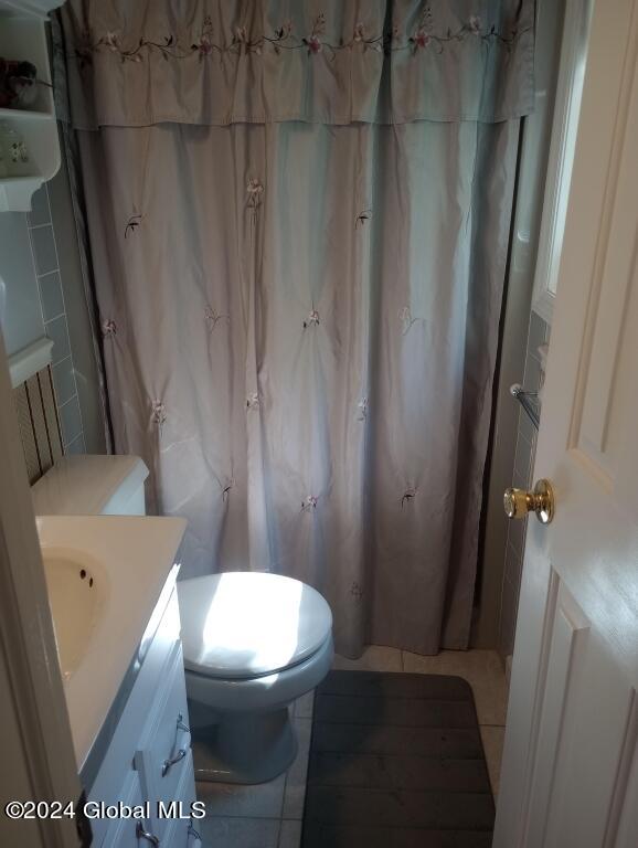 bathroom with a shower with shower curtain, tile patterned floors, vanity, and toilet