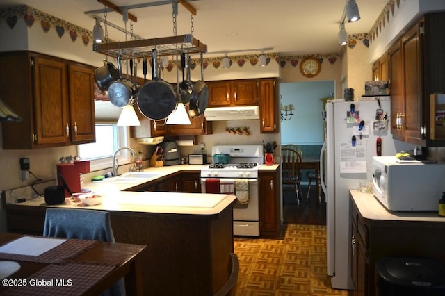 kitchen featuring white appliances, a sink, under cabinet range hood, a peninsula, and light countertops