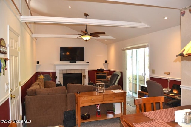 living room with ceiling fan, a tile fireplace, and a wainscoted wall