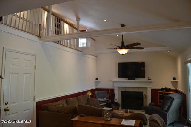 living area featuring ceiling fan, a fireplace, and a wainscoted wall